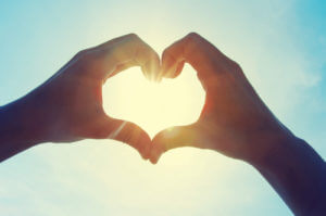 a person makes a heart out of their hands and holds it up to the sun