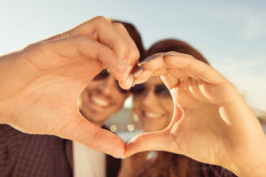 a couple poses through a heart they are making with their hands