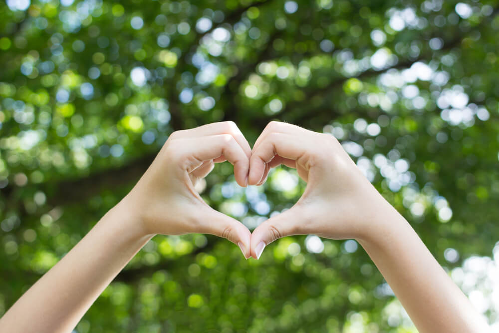 a woman makes a heart with her hands to represent self compassion