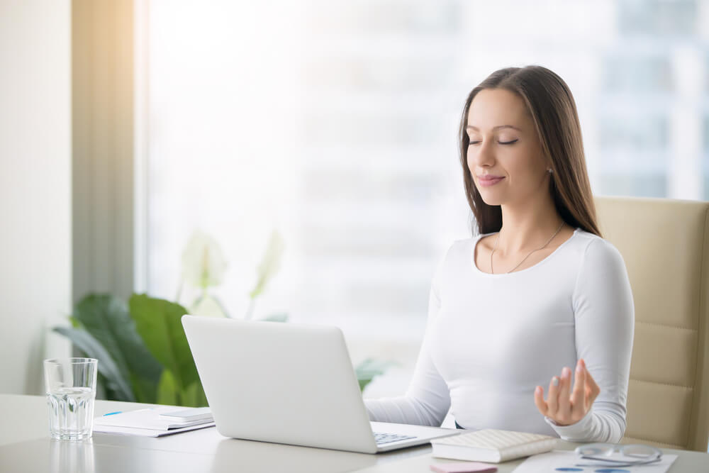 a woman meditates at her desk to manage mental health at work