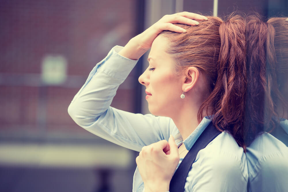 a burnt out woman holds her hand to her head and looks stressed