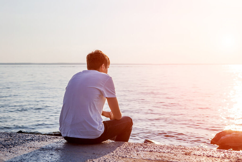 Man sitting on a beach struggling with PTSD and addiction